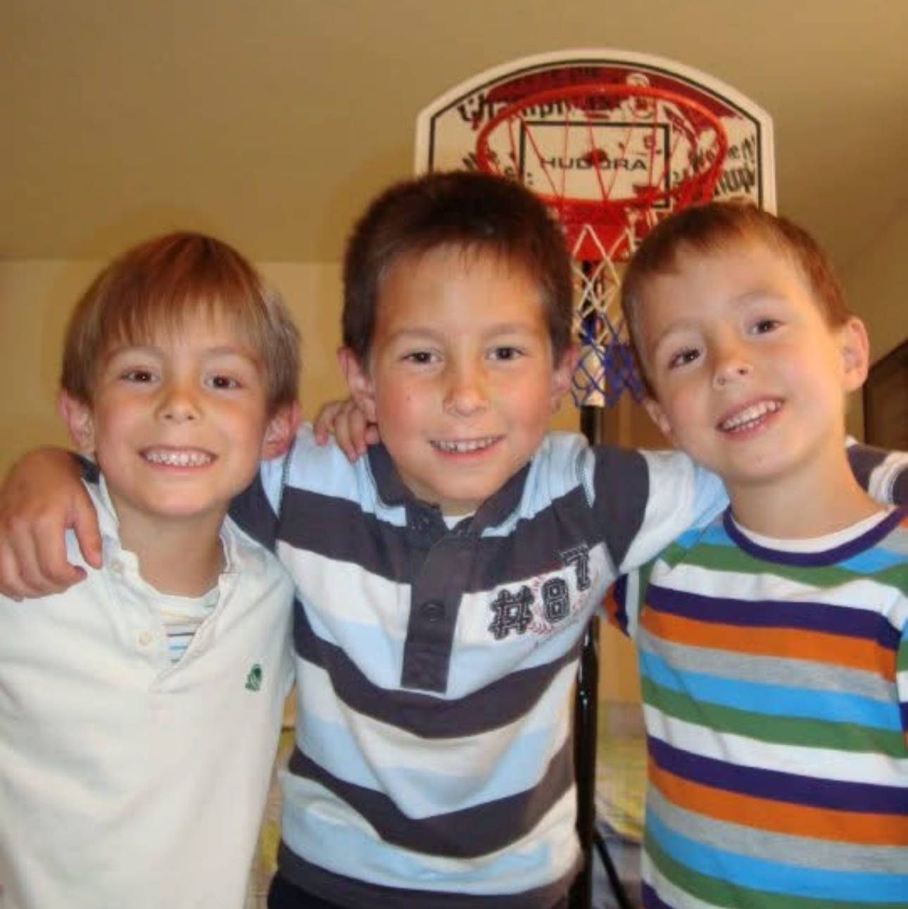 Three children posing together in front of a basketball hoop.